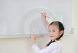 Portrait of happy little Asian child girl or Schoolgirl writing something on whiteboard with a marker and looking at camera in the