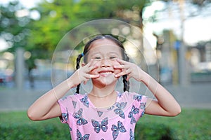 Portrait of happy little Asian child girl show finger in shape of look like a cat on her face in the garden