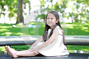 Portrait of happy little Asian child girl sitting on bench in sunny green park