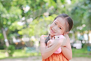 Portrait of happy little Asian child in green garden with hugging teddy bear and looking at camera. Close up smiling kid girl in