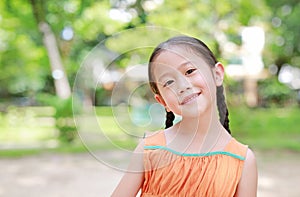 Portrait of happy little Asian child in green garden with looking at camera. Close up smiling kid girl in summer park