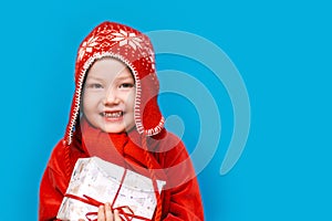 Portrait of a happy little boy holding a new christmas gift with red ribbon in red clothes. happy new year, merry christmas