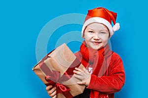 Portrait of a happy little boy holding a new christmas gift with red ribbon in red clothes. happy new year, merry christmas