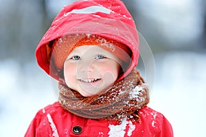 Portrait of happy little boy in red winter clothes having fun during snowfall