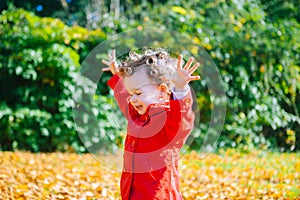 Portrait of happy little child, baby girl laughing and playing with leaves in the autumn park