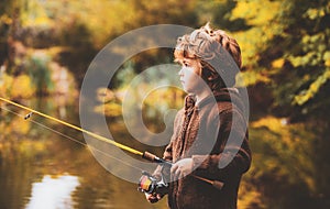 Portrait of happy little child son fishing on river with spinning reel. Happy kids autumn weekend concept.