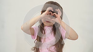 A portrait happy little girl child with brown hair smiles and holding heart shaped her hands on eyes. Health of eyes and
