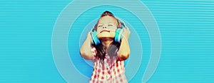 Portrait of happy little girl child in wireless headphones listening to music on blue background, blank copy space for advertising