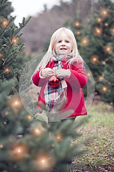 Portrait of happy little girl hanging bauble on tree outdoors