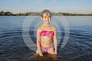 A portrait of a happy little girl in the river, on a sunny day, at sunset.  A child in a bathing suit