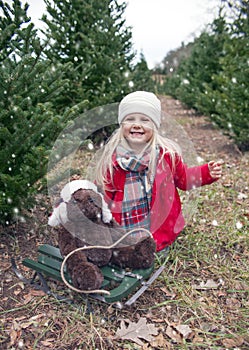 Portrait of happy little girl sitting with teddy bear on sled