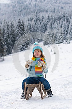 Portrait of happy little kid wearing knitted hat, scarf and sweater. Kid boy enjoying a sleigh ride. Child sledding