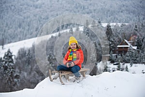 Portrait of happy little kid wearing knitted hat, scarf and sweater. Kid boy enjoying a sleigh ride. Winter fun kids