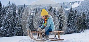 Portrait of happy little kid wearing knitted hat, scarf and sweater. Kid boy enjoying a sleigh ride on winter landscape