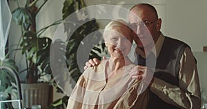 Portrait of happy lovely romantic 70s senior husband and wife, retired couple hugging, smiling looking at camera at home