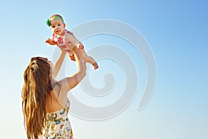 Portrait of happy loving mother and her baby outdoors. Mother and child against summer blue sky.
