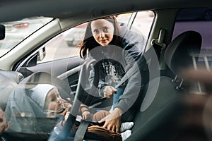 Portrait of happy loving young mother putting child safety seat with infant baby boy on front passenger seat with back