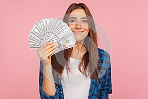 Portrait of happy lucky girl in checkered shirt holding lot of money and smiling to camera, showing dollar bills