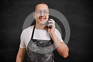 Portrait of a happy male chef with a phone in his hands, looking at the camera on a dark background