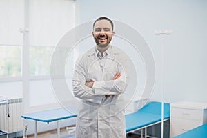 Portrait of a happy male doctor standing with arms crossed at medical office