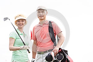 Portrait of happy male and female golfers standing against clear sky