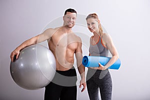 Male And Female Sports Person Holding Exercise Ball And Mat