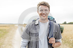 Portrait of happy male hiker with backpack standing on field