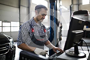 Portrait of happy male mechanic touching computer monitor in auto repair shop