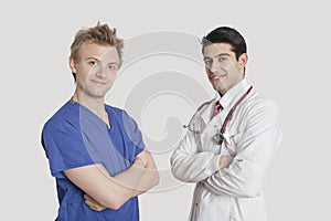 Portrait of happy male nurse and doctor standing with arms crossed over gray background