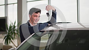 portrait of happy male owner of new car with keys in his hands in automobile dealership, smiling and looking at camera