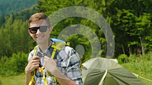 Portrait of a happy male traveler. Smiling, looking at the camera, standing near the tent in the camping