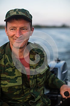 Portrait of a happy man in camouflage driving a motor boat.