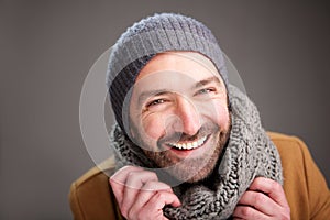 Happy man with hat and scarf posing against gray wall