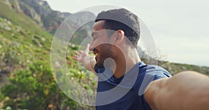 Portrait of a happy man hiking and pointing to the scenic views while taking selfies and making a video call. Face a