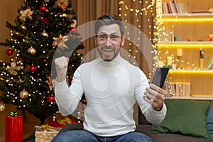 Portrait of happy man at home for christmas, businessman phone celebrating victory and success good news online