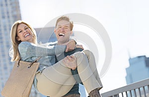 Portrait Of Happy Man Lifting Woman In City