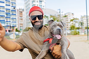 portrait of happy man in red hat and sunglasses with american terrier in dogs walking area park in sity