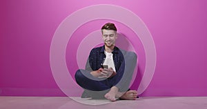 Portrait of a happy man using mobile phone isolated over pink background.