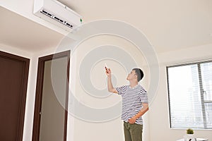 Portrait Of Happy Man Using Remote Control To Operate Air Conditioner