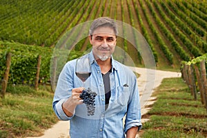 Portrait of happy man in vineyard with glass of wine