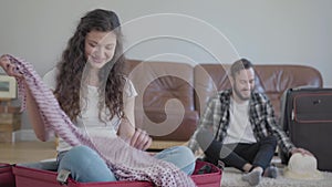 Portrait happy man and woman on the floor packing a suitcase before travel at home. The wife throwing things up, sitting