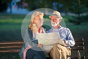 Portrait of happy man and woman reading map while sitting on a park bench. Senior couple on vacation using city map.