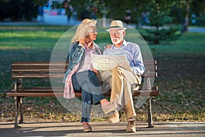 Portrait of happy man and woman reading map while sitting on a park bench. Senior couple on vacation using city map.