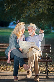 Portrait of happy man and woman reading map while sitting on a park bench. Senior couple on vacation using city map.