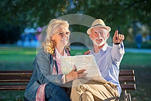 Portrait of happy man and woman reading map while sitting on a park bench. Senior couple on vacation using city map.