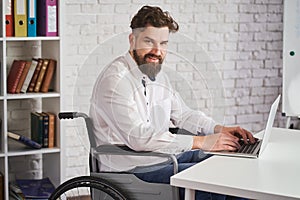 Portrait of a happy man working on a laptop and sitting on a wheelchair