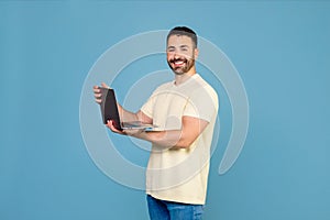 Portrait of happy man working online remote, using new laptop computer, smiling at camera, blue background