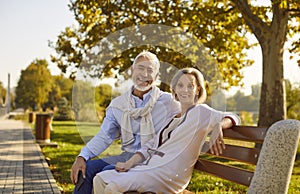 Portrait of happy married senior couple sitting on bench in beautiful green summer park