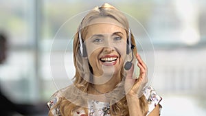 Portrait of a happy mature blonde female customer support operator in headset.