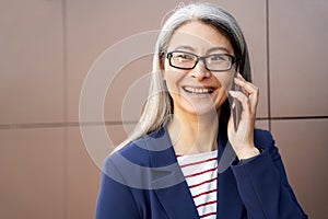 Portrait of a happy mature business woman wearing eyeglasses and classic wear talking on mobile phone and smiling while